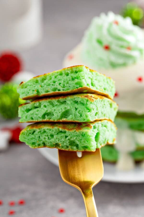 These fluffy Grinch Pancakes with cream cheese frosting are an easy homemade Christmas pancake recipe for a festive Christmas breakfast! A fork holding up a bite of fluffy green Christmas pancakes.