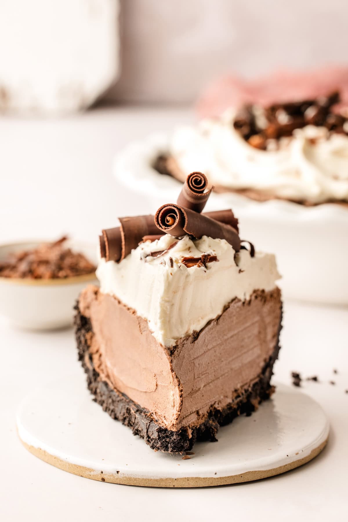 This French Silk Pie recipe has the silkiest, rich chocolate filling, with a crisp Oreo crust, and a cloud of sweet whipped cream on top. A thick slice of French silk pie is presented on a small white plate.
