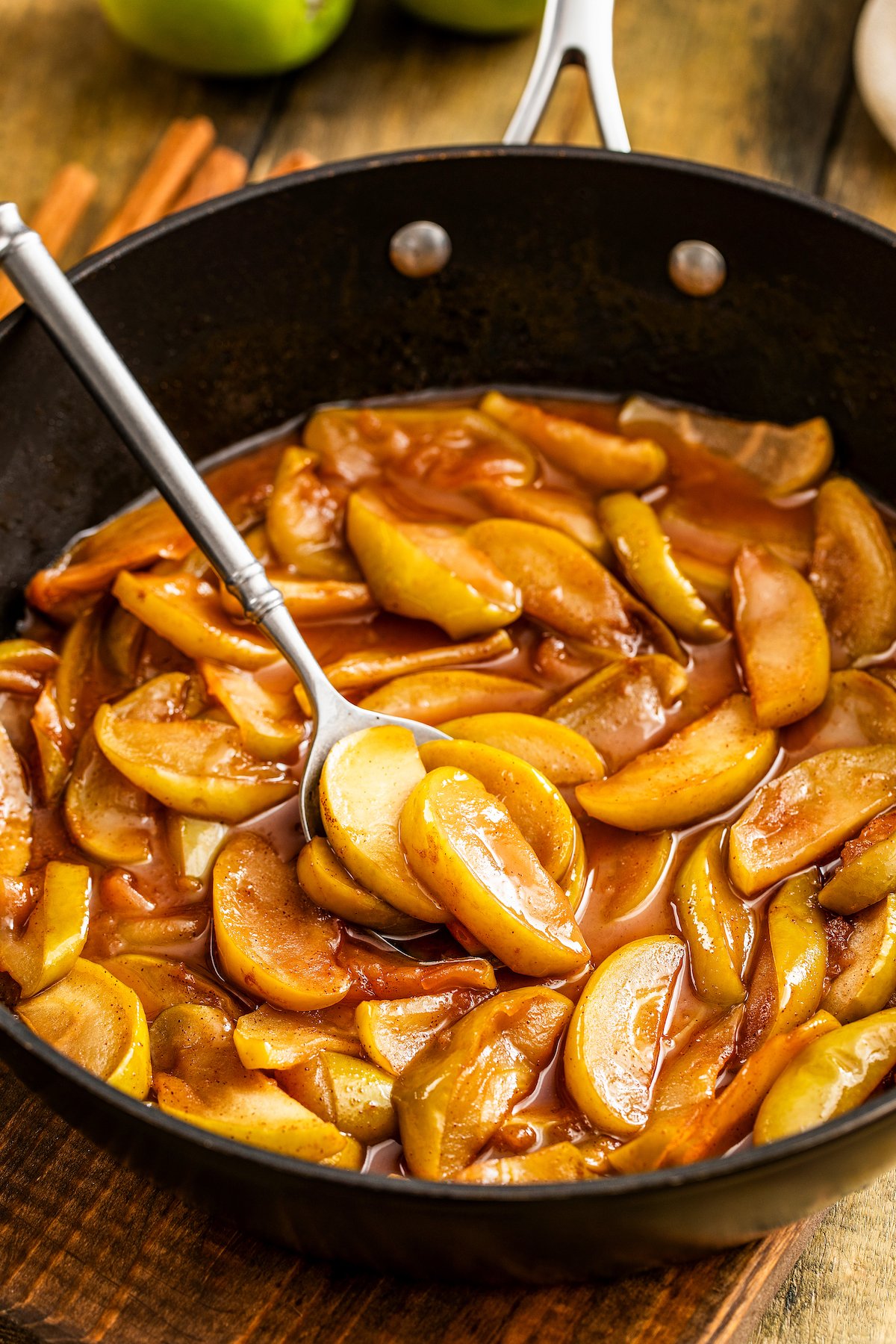 This easy, southern-style Cracker Barrel Fried Apples recipe creates the best tender apples in a comforting cinnamon and brown sugar sauce. Showing how to make fried apples in a skillet with a spoon stirring the apples.