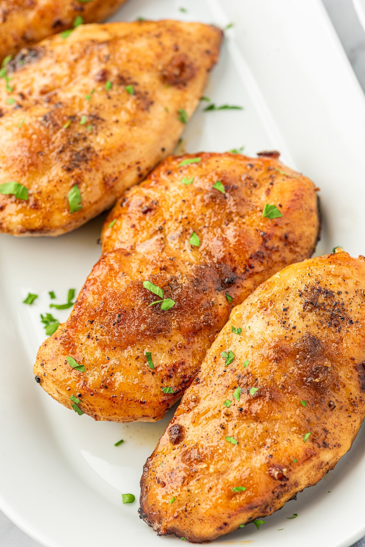 This tender and juicy garlic brown sugar chicken recipe is an easy sweet and savory dinner. You only need 4 ingredients and 25 minutes! Tender and juicy garlic brown sugar chicken breasts on a serving plate topped with fresh herbs.