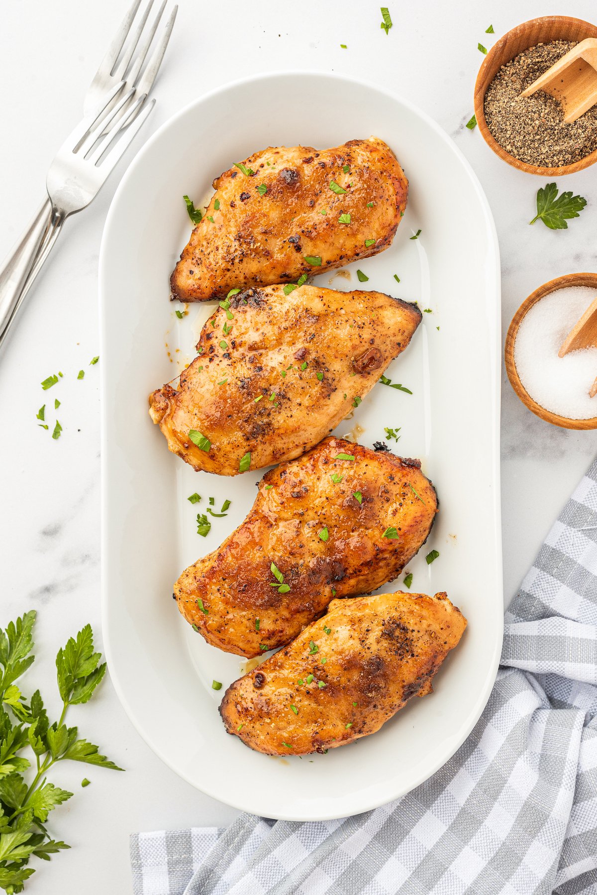 This tender and juicy garlic brown sugar chicken recipe is an easy sweet and savory dinner. You only need 4 ingredients and 25 minutes! Four juicy brown sugar chicken breasts on a serving platter topped with fresh herbs.