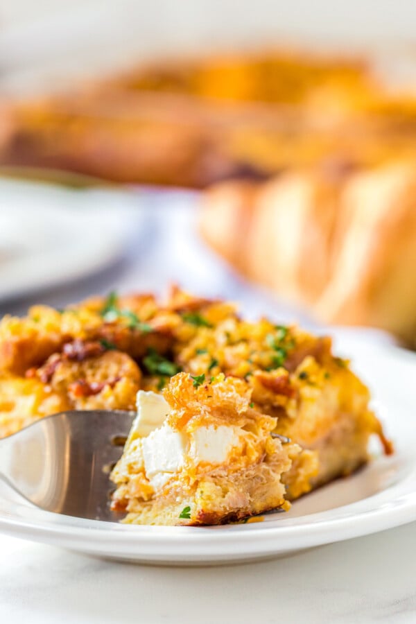 This overnight breakfast casserole with ham is made with flaky croissants, cream cheese and a crispy, buttery cornflake topping for crunch! A fork cutting a bite of Ham Breakfast Casserole.