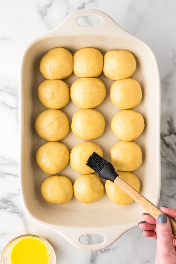 Soft & buttery Hawaiian Rolls are golden in color with a sweet hint of pineapple flavor. This homemade yeast roll recipe is a crowd favorite! Balls of yeast dough in a baking dish being brushed with egg wash.