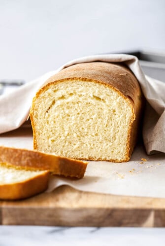 Loaf of homemade bread sliced on a cutting board with a tea towel.