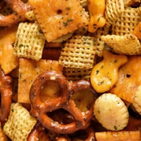 A close-up of homemade Chex Mix, featuring Chex cereal, pretzels, cheese crackers, round crackers, and goldfish crackers.