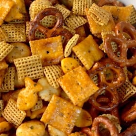 A close-up of a bowl of homemade chex mix including pretzels, Chex cereal, cheese crackers, and goldfish crackers, all seasoned and mixed together.