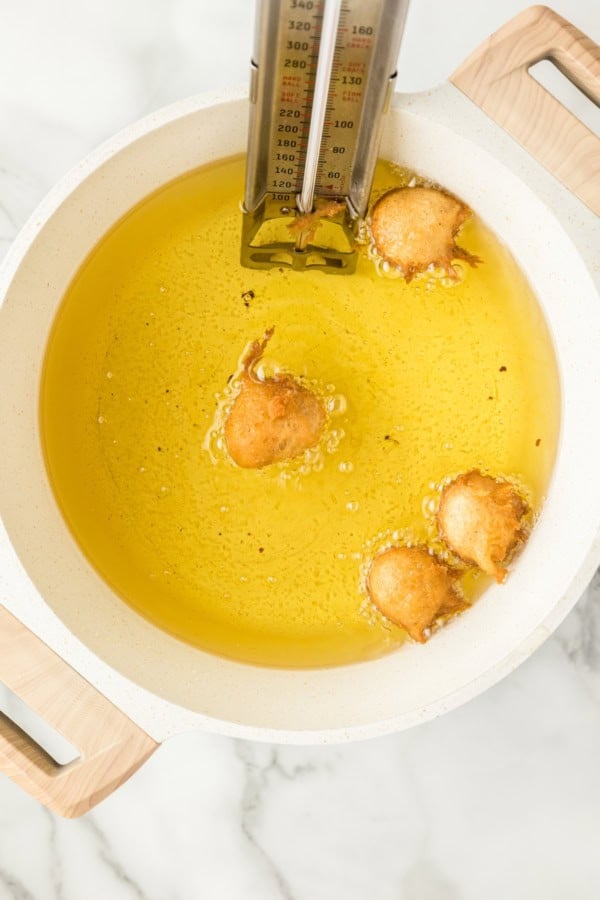 Fresh warm Donut Holes in just 20 minutes — with no yeast or fancy equipment needed! Perfect for dunking, glazing, or stuffing with fillings. Golden brown donut holes are being deep-fried in a pot of hot oil, with a thermometer clipped to the side indicating the temperature.