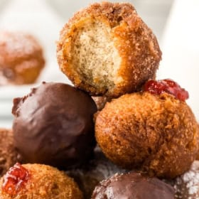 A plate of homemade donut holes, some dusted with sugar and others coated in chocolate. One donut hole is bitten to show its fluffy interior.