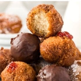 A stack of homemade donut holes with a mix of sugar-coated, chocolate-covered, and jelly-filled varieties. The top donut has a bite taken out of it.
