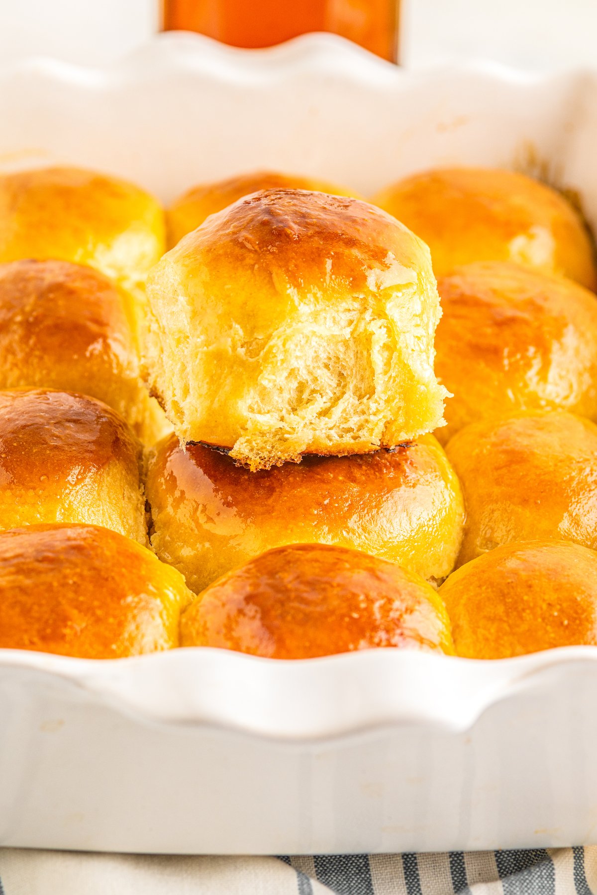 Soft & buttery Hawaiian Rolls are golden in color with a sweet hint of pineapple flavor. This homemade yeast roll recipe is a crowd favorite! A white baking dish full of Hawaiian dinner rolls. One soft and sweet yeast roll is sitting on top of the rest.