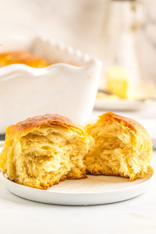 Soft & buttery Hawaiian Rolls are golden in color with a sweet hint of pineapple flavor. This homemade yeast roll recipe is a crowd favorite! A sweet Hawaiian rolls torn in half on a plate to show the tender texture of the interior.