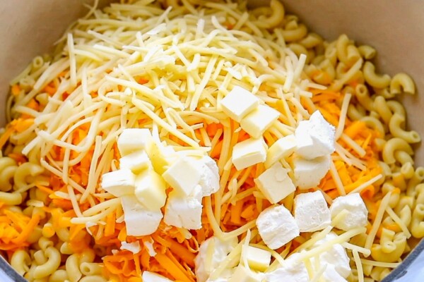 This easy, one-pot homemade mac and cheese recipe is made extra creamy with three types of cheese! Bonus: It's ready in under 20 minutes. Shredded cheese and cream cheese is being mixed into cooked noodles.