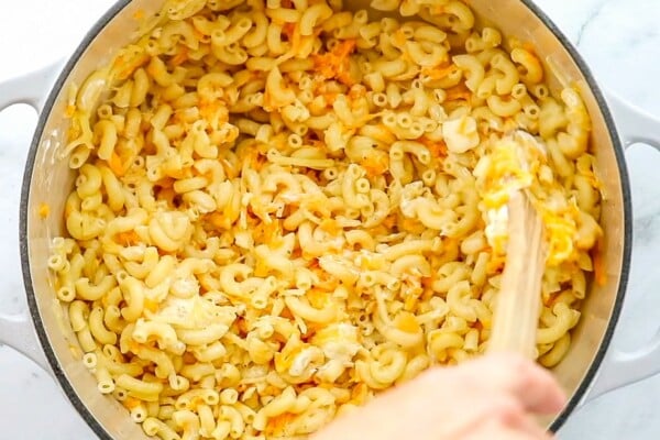 This easy, one-pot homemade mac and cheese recipe is made extra creamy with three types of cheese! Bonus: It's ready in under 20 minutes. Elbow macaroni noodles are being mixed in a pot with more mac and cheese ingredients.