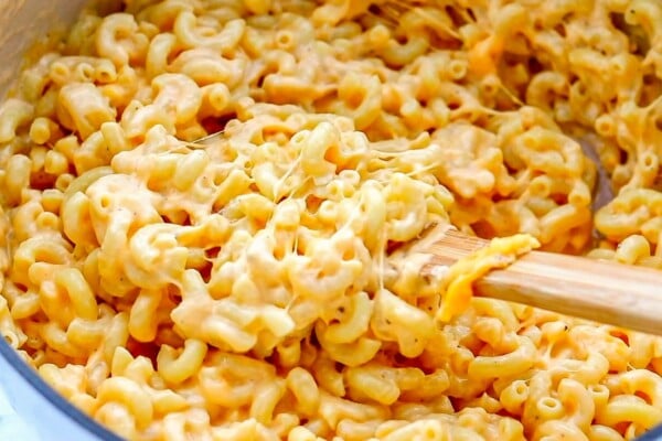 This easy, one-pot homemade mac and cheese recipe is made extra creamy with three types of cheese! Bonus: It's ready in under 20 minutes. Creamy mac and cheese is being stirred in a pot.