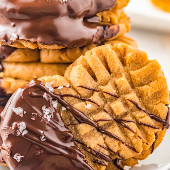 A closeup shot of a homemade Nutter Butter cookie, generously topped with chocolate. In the background are several more of the cookies, stacked on a plate.