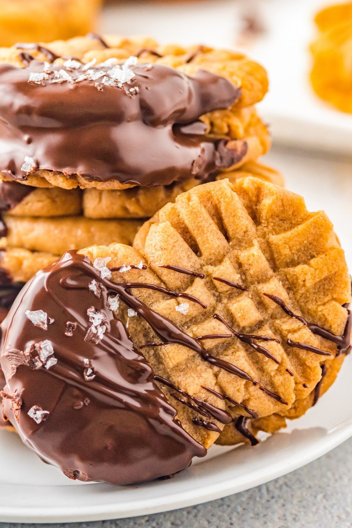 A closeup shot of a homemade Nutter Butter cookie, generously topped with chocolate. In the background are several more of the cookies, stacked on a plate.