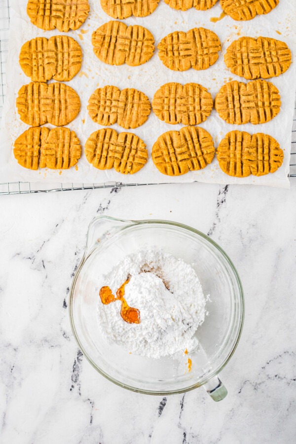 A baking sheet with baked Nutter Butter cookies lies near a mixing bowl with the Nutter Butter filling ingredients inside.