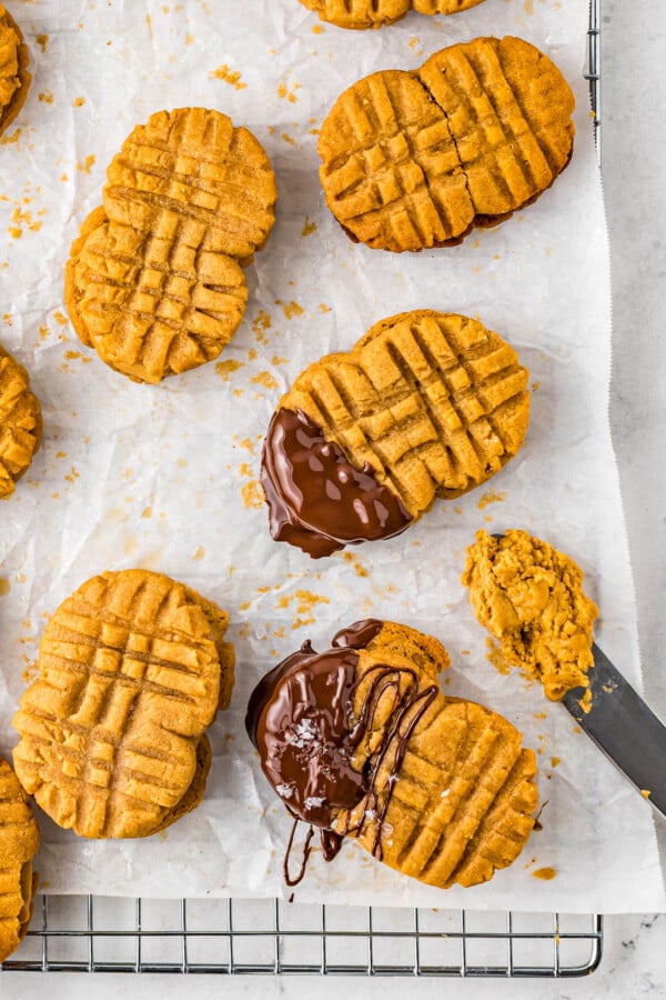 Several Nutter Butter sandwich cookies, two dipped in chocolate and four plain. A knife with peanut butter filling on the end lies nearby.