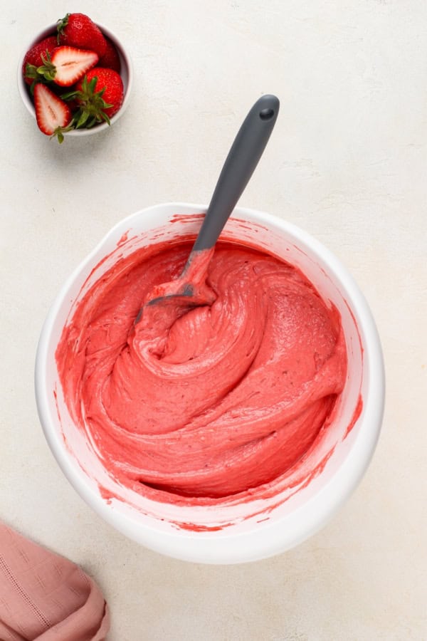 With a soft, tender crumb, this Homemade Strawberry Cake is made entirely from scratch with fresh berries and a creamy strawberry frosting! Pink cake batter is being mixed in a large white bowl.