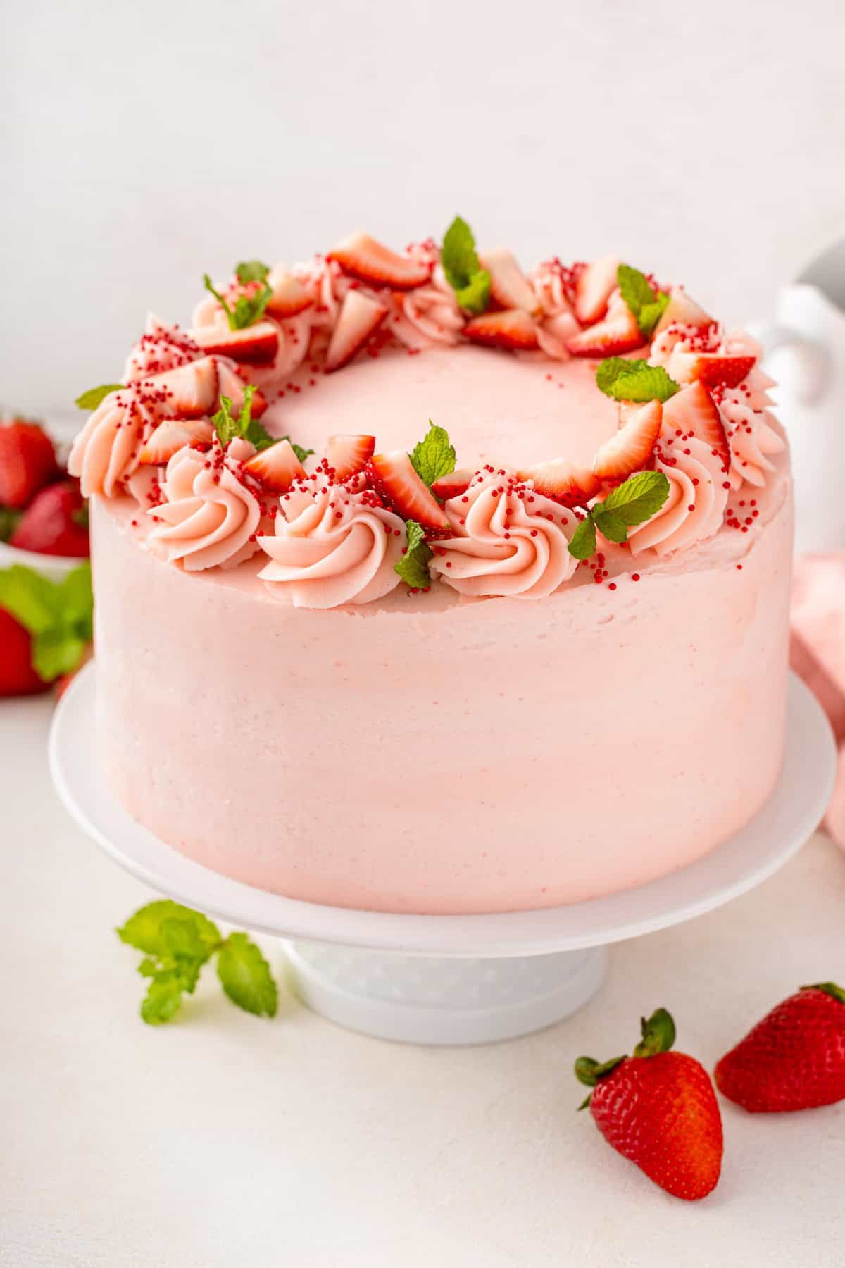 With a soft, tender crumb, this Homemade Strawberry Cake is made entirely from scratch with fresh berries and a creamy strawberry frosting! A frosted fresh strawberry cake is garnished with fresh berries.