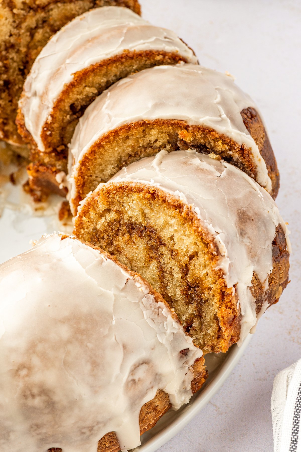 Honey Bun Cake is a spin on classic honey buns. You'll love this tender and moist, cinnamon-swirled bundt cake topped with a sugary glaze. Sliced honey bun cake with glaze on a cake plate.