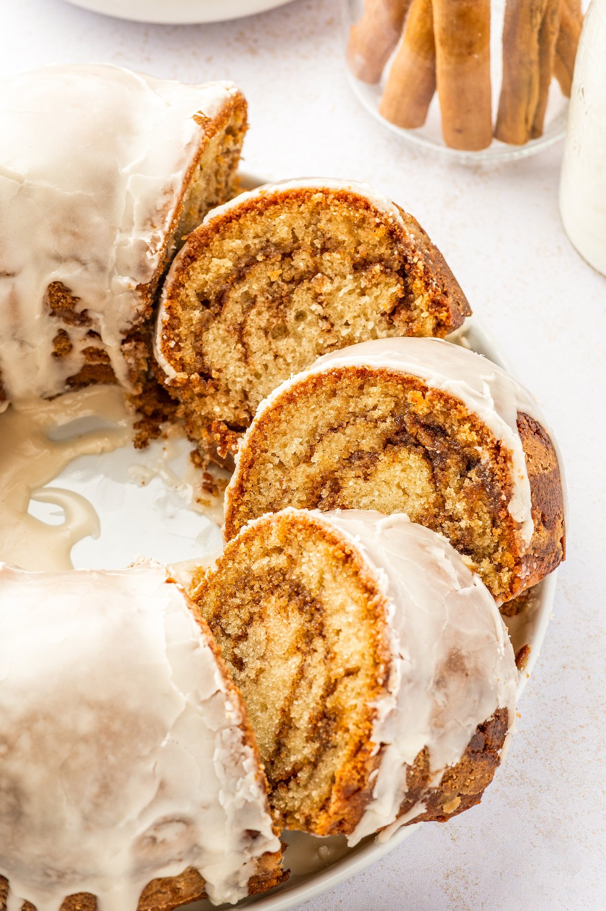 Honey Bun Cake is a spin on classic honey buns. You'll love this tender and moist, cinnamon-swirled bundt cake topped with a sugary glaze. Slices of cake fanned out on a platter, with the rest of the cake unsliced.