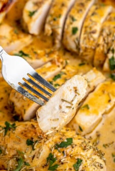 A fork lifting a piece of sliced chicken breast out of a baking dish of baked chicken.