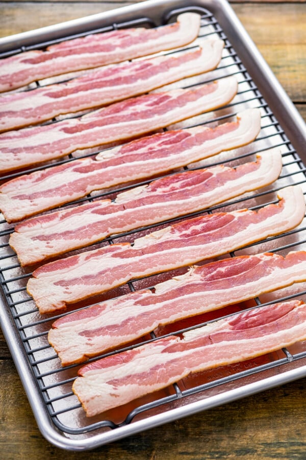 Whether you like it extra crispy or slightly tender, here are two mess-free ways for how to cook bacon in the oven to perfection, every time! Showing how to cook crunchy bacon in the oven by lining strips of uncooked bacon lined on top of a wire rack over a baking sheet.