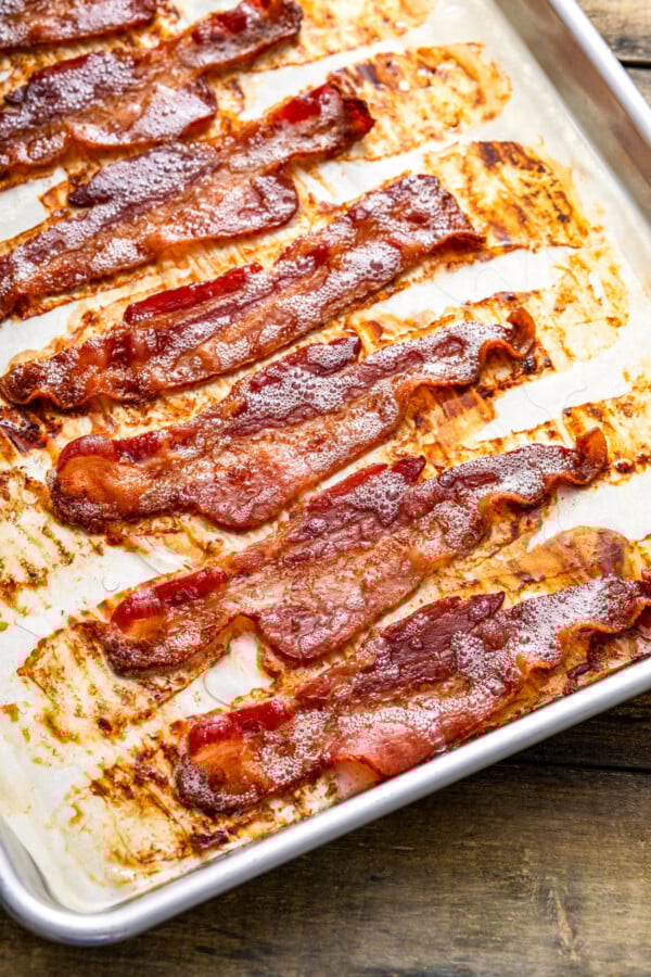 Whether you like it extra crispy or slightly tender, here are two mess-free ways for how to cook bacon in the oven to perfection, every time! Cooked bacon arranged on a baking sheet with parchment paper to show how to make bacon in the oven without a wire rack.