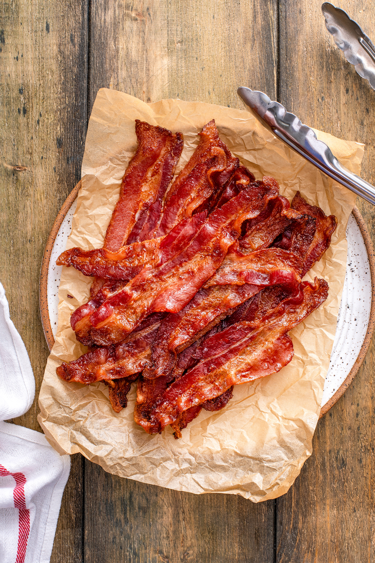 Whether you like it extra crispy or slightly tender, here are two mess-free ways for how to cook bacon in the oven to perfection, every time! Crispy, smokey oven bacon on a plate lined with parchment paper.