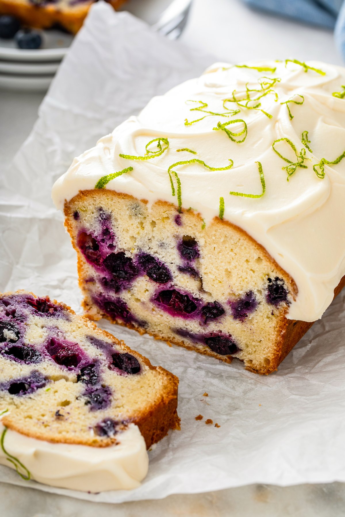 This moist and tender Lime Blueberry Pound Cake is bursting with fresh blueberries and lime zest with a thick cream cheese frosting on top! A sweet and dense lime blueberry pound cake topped with a thick layer of cream cheese frosting being sliced into pieces.