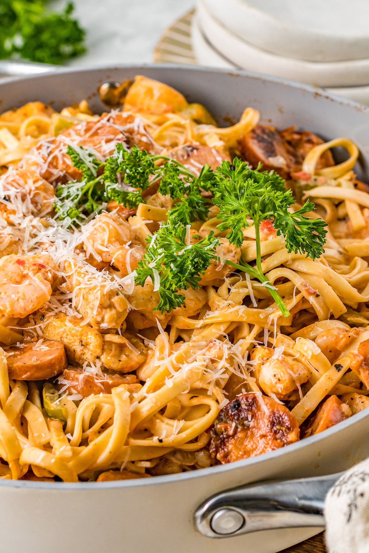 Featuring chicken, sausage, and shrimp, this creamy Cajun Pasta recipe is tossed in a creamy and spicy sauce with tender linguine pasta. A large cooking pot of creamy Cajun pasta with fresh herbs and parmesan cheese sprinkled on top.