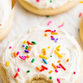 A bite taken out of a cookie with frosting and sprinkles.