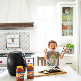 A baby boy is laughing while holding two slices of eggplant