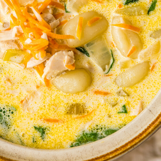 Gnocchi, chicken, and shredded carrots cooking in a creamy broth.