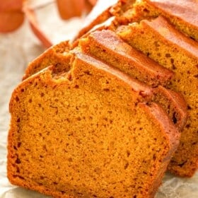 Sliced loaf of golden brown pumpkin bread on parchment paper, showing a moist, dense texture.