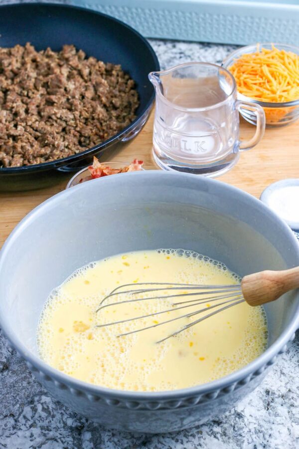 A blue mixing bowl with a whisk with eggs and milk