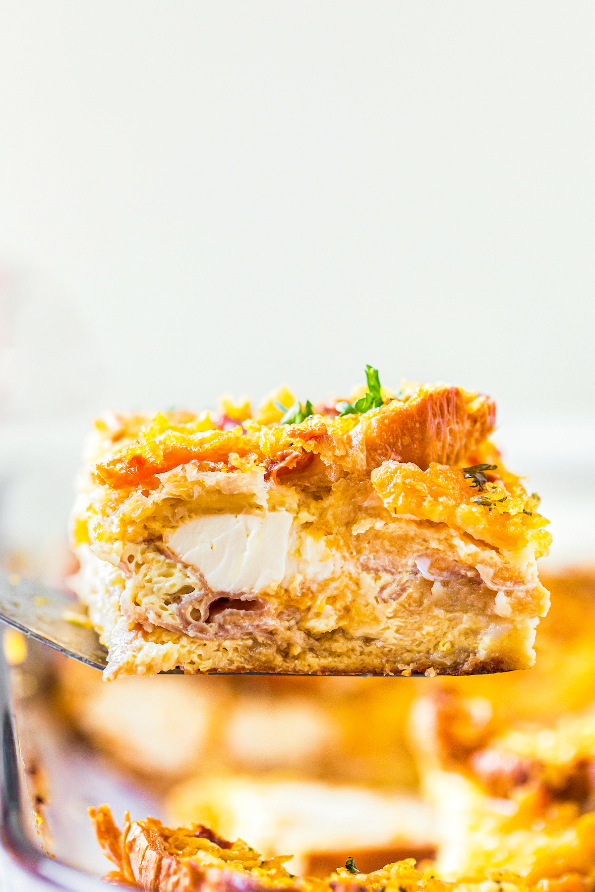 This overnight breakfast casserole with ham is made with flaky croissants, cream cheese and a crispy, buttery cornflake topping for crunch! A serving of Overnight Breakfast Casserole with Ham being lifted out of a casserole dish with a spatula.