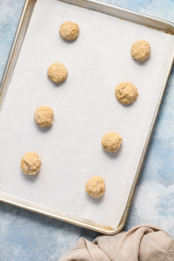 With a hint of cinnamon, crisp edges, and a chewy center, these wholesome Peanut Butter Oatmeal Cookies are sure to please! Balls of cookie dough lined up on a parchment-lined cookie sheet.