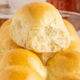 A soft dinner roll resting on top of more dinner rolls in a glass baking sheet.