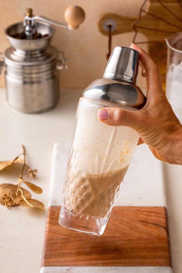 Smooth, spiced, and perfectly creamy, this Pumpkin Espresso Martini fall in a glass. Made with real pumpkin, espresso, and RumChata! A hand shaking a cocktail shaker filled with a pumpkin martini.