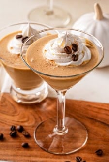 A martini glass filled with a creamy pumpkin espresso martini, topped with whipped cream, a sprinkle of pumpkin pie spice, and coffee beans.