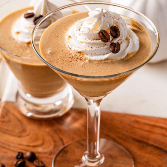 A martini glass filled with a creamy pumpkin espresso martini, topped with whipped cream, a sprinkle of pumpkin pie spice, and coffee beans.