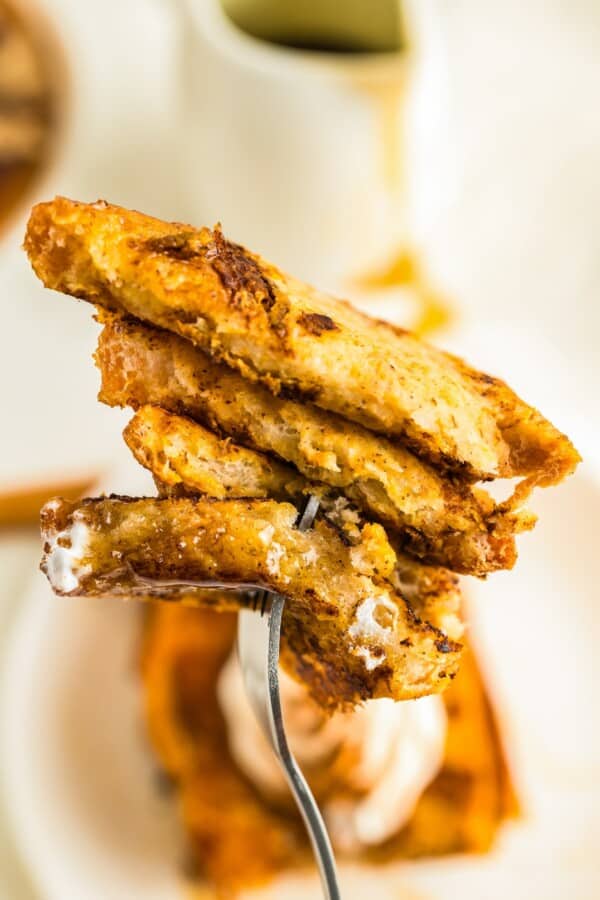 Packed with pumpkin pie flavor, this quick and easy pumpkin French toast, served with maple syrup or powdered sugar, will disappear quickly! A fork is piercing a bite sized portion of pumpkin French toast.