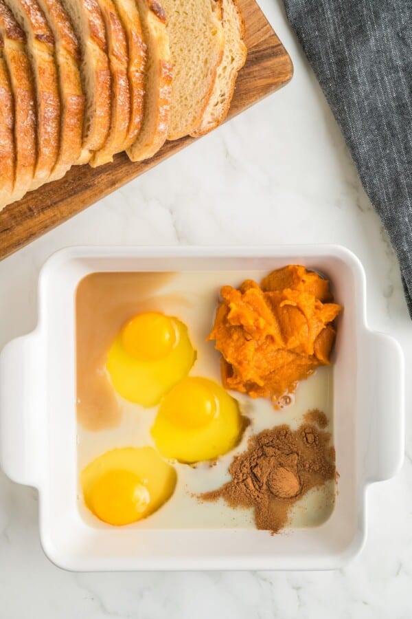 Packed with pumpkin pie flavor, this quick and easy pumpkin French toast, served with maple syrup or powdered sugar, will disappear quickly! Slices of bread are next to a baking dish with ingredients in it.