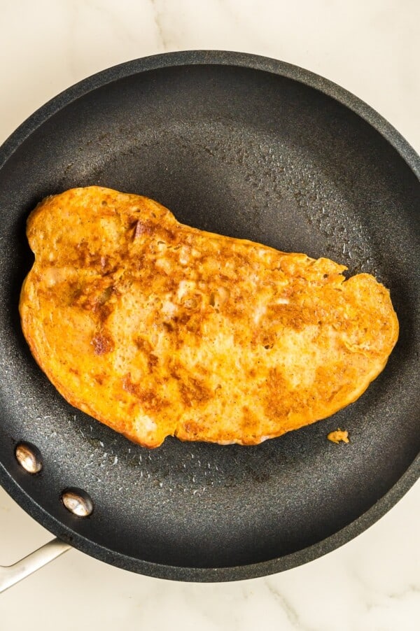 Packed with pumpkin pie flavor, this quick and easy pumpkin French toast, served with maple syrup or powdered sugar, will disappear quickly! A piece of battered toast is cooking in a skillet.