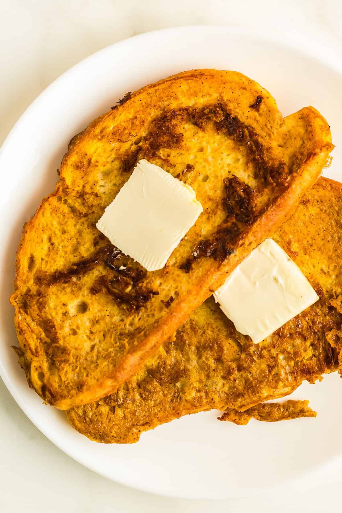 Packed with pumpkin pie flavor, this quick and easy pumpkin French toast, served with maple syrup or powdered sugar, will disappear quickly! Slices of butter are placed on top of homemade pumpkin French toast.