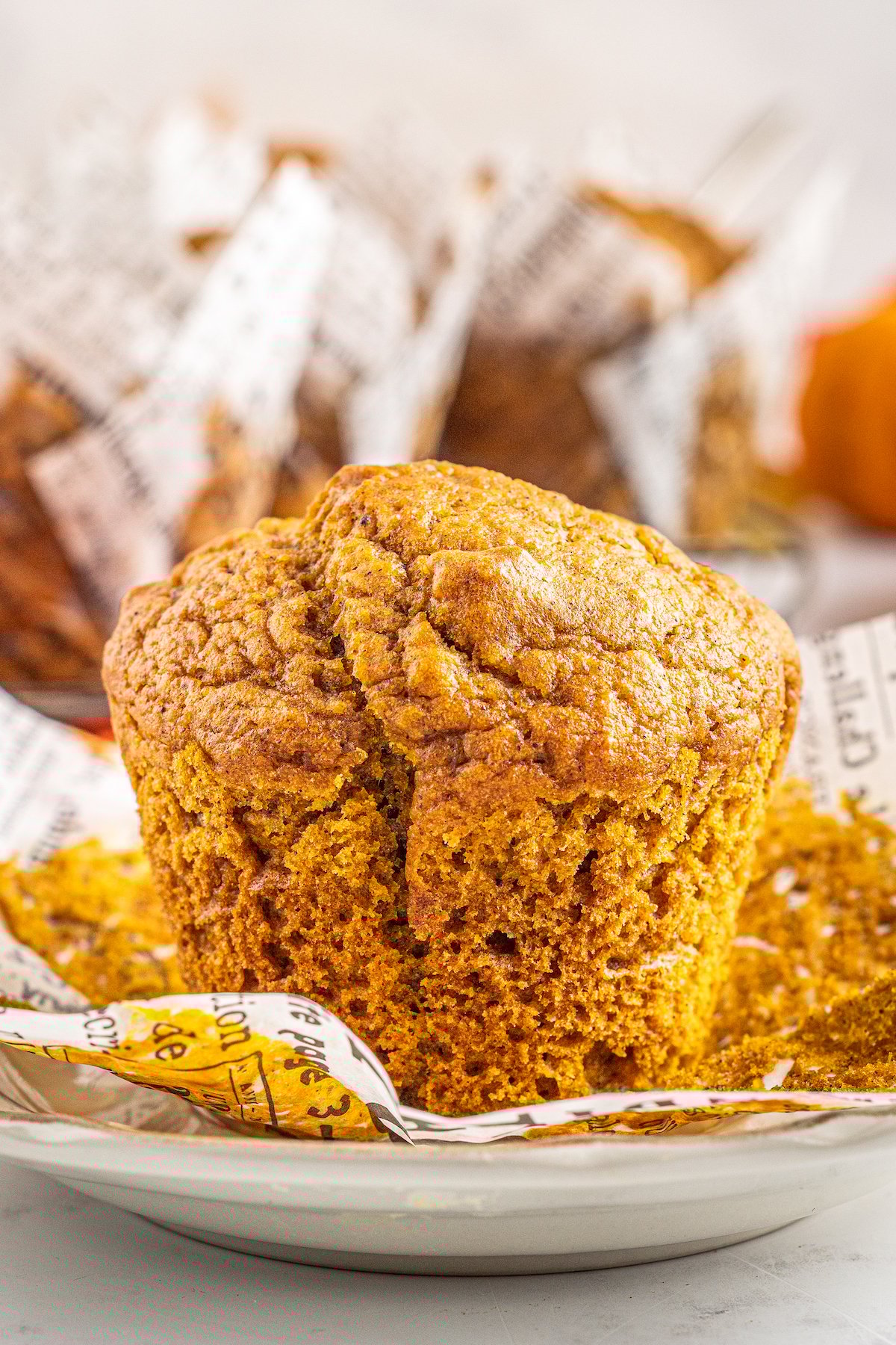 This bakery-style easy pumpkin muffin recipe creates moist and tender muffins made with a whole can of pumpkin and warm autumn spices! A pumpkin muffin with no wrapper is placed on a plate.