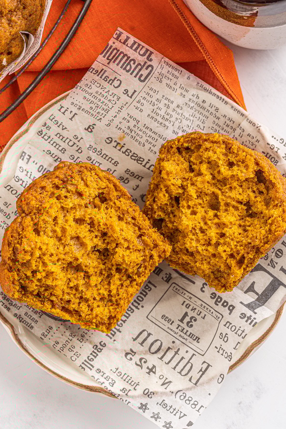 This bakery-style easy pumpkin muffin recipe creates moist and tender muffins made with a whole can of pumpkin and warm autumn spices! A pumpkin muffin has been split in half and presented on a wrapper.