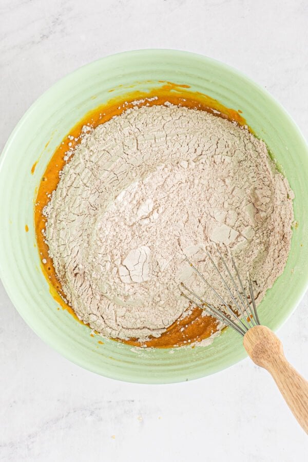 This bakery-style easy pumpkin muffin recipe creates moist and tender muffins made with a whole can of pumpkin and warm autumn spices! Dry muffin ingredients being whisked into wet muffin ingredients.